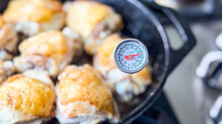 Instant read thermometer at 165 F inserted in chicken thigh in cast iron skillet