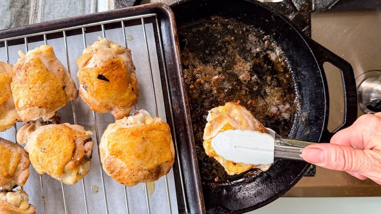 Placing browned chicken thighs on rack to rest using tongs