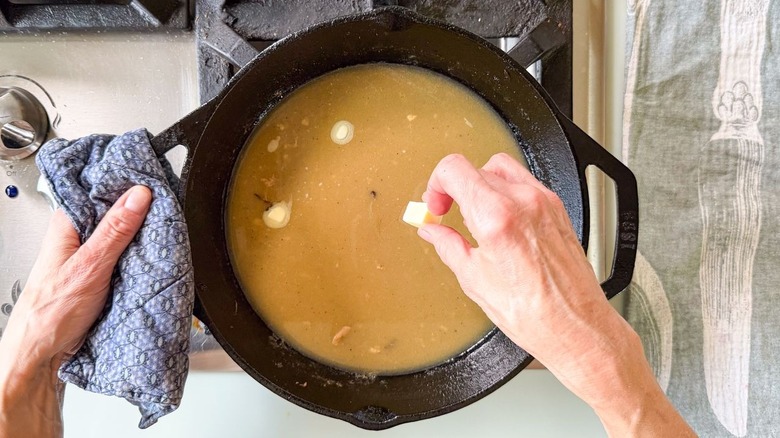 Swirling cubes of cold butter into sauce in cast iron skillet to emulsify