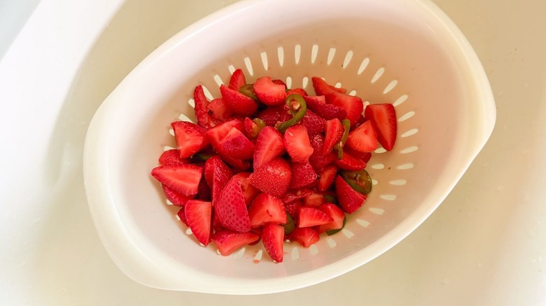 Draining pickled strawberries and jalapeños in colander in sink