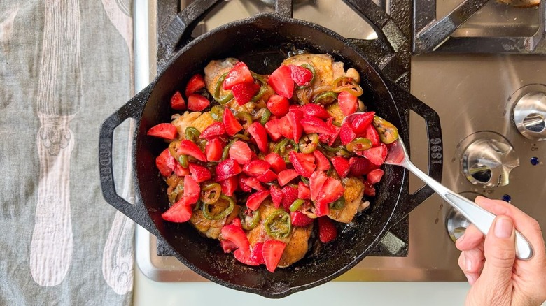 Spooning pickled strawberries and jalapeños over chicken thighs in cast iron skillet on stovetop