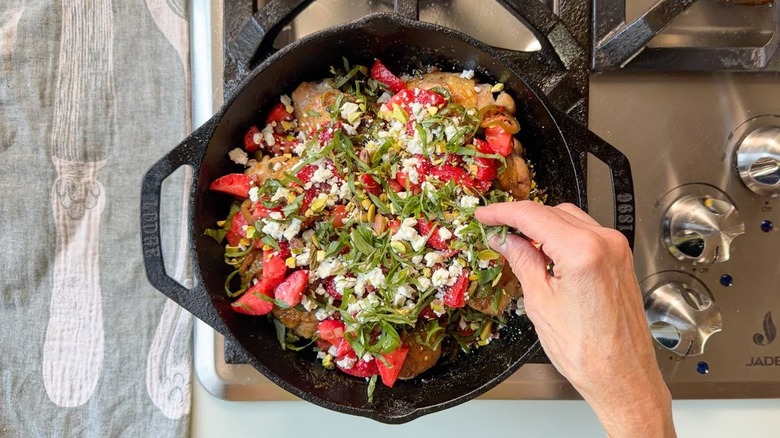 Garnishing strawberry jalapeño chicken with crispy pancetta, crumbled goat cheese, pistachios, and slivered basil in cast iron skillet
