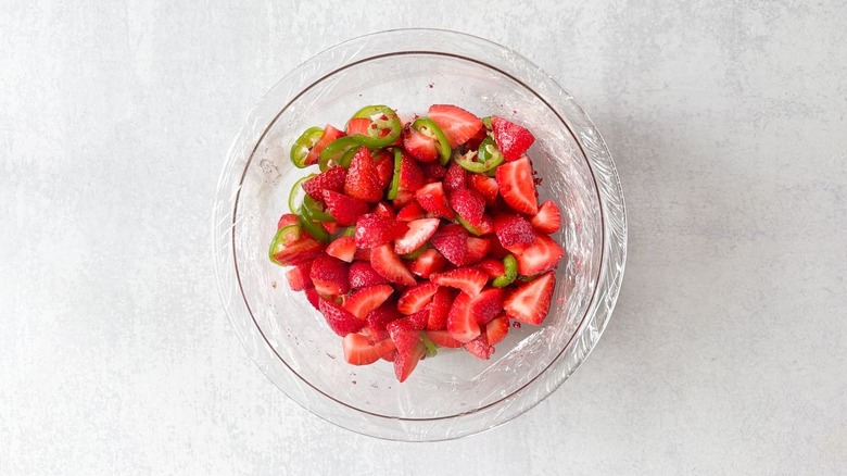 Pickled strawberries and jalapeños in plastic-covered glass bowl