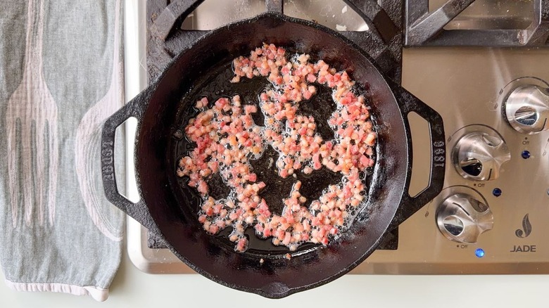 Crispy pancetta cooking in cast iron skillet on stovetop