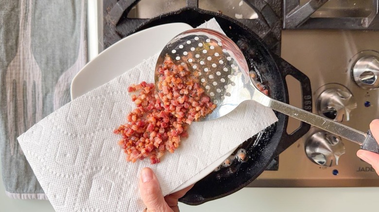 Moving crispy pancetta from cast iron skillet to paper towel-lined plate with slotted spoon