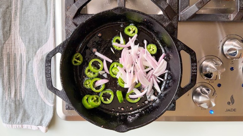 Sliced jalapeños and shallots in cast iron skillet on stovetop