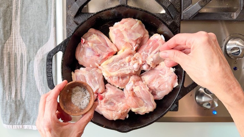 Seasoning skin-side-down chicken thighs in cast iron skillet on stovetop
