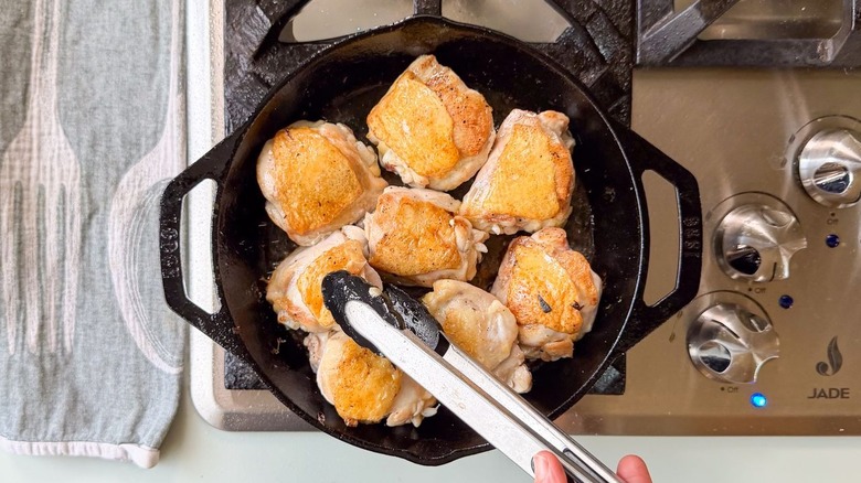 Chicken thighs with golden brown skin cooking in cast iron skillet