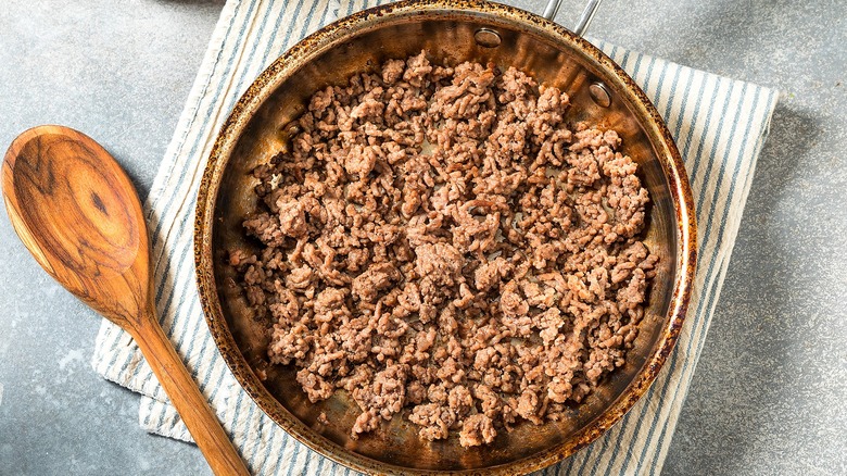 Top-down view of cooked ground beef in a metal frying pan over a striped dish cloth