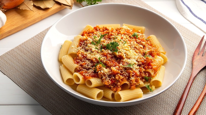 Rigatoni pasta topped with a meat-based tomato sauce and grated parmesan cheese in a shallow white bowl