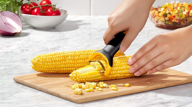 Hands peel kernels off of corn using the OXO corn stripper