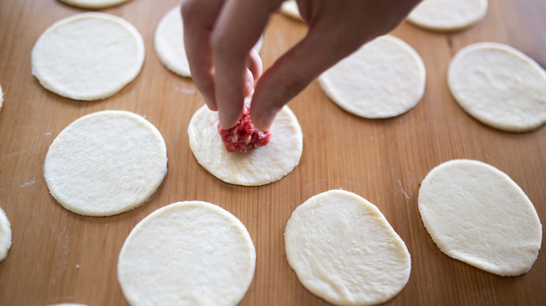 A hand filling small dough rounds
