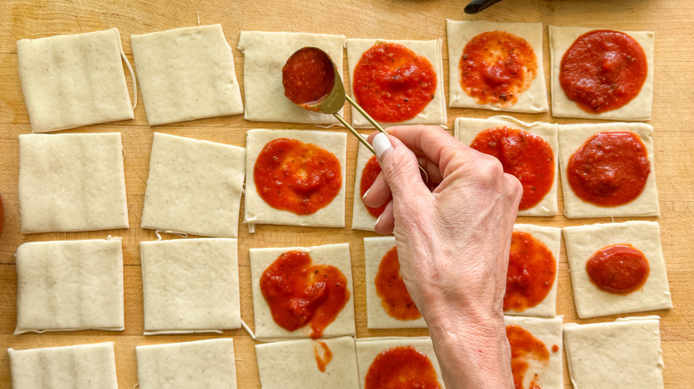hand adding sauce to dough squares