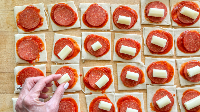 hand adding cheese to pizza dough squares