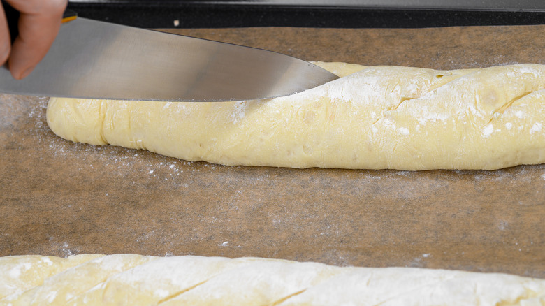 Cook making cuts on surface of baguette dough.