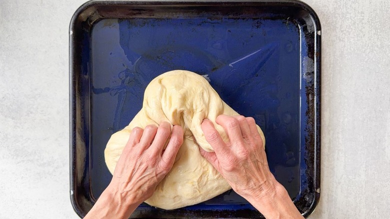 Shaping focaccia dough on oiled blue baking sheet