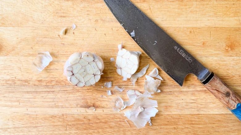 Garlic head with top sliced off on cutting board
