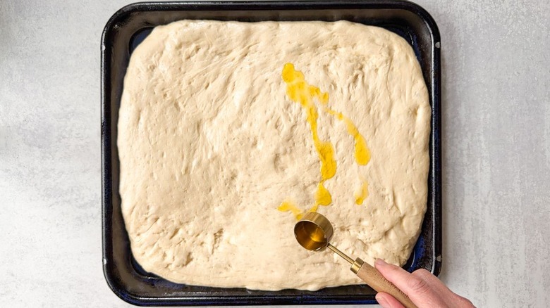 Drizzling olive oil over puffy focaccia dough