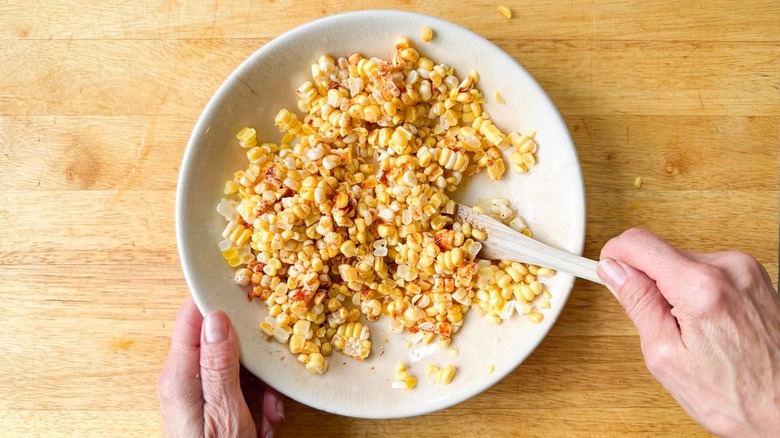 Seasoning raw corn kernels with spices and olive oil in shallow bowl