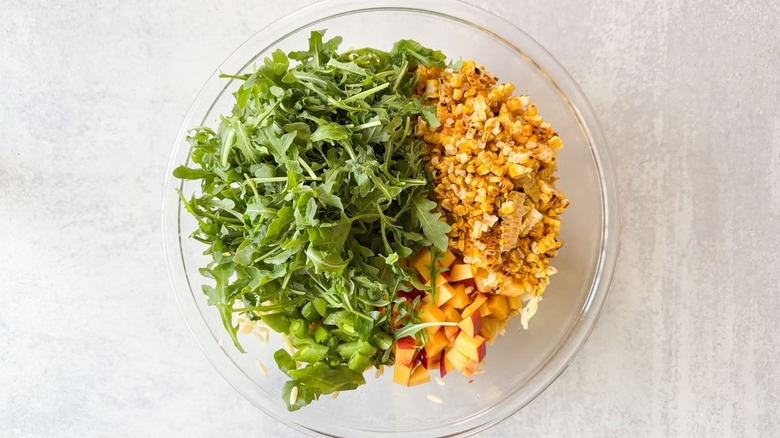 Baby arugula, grilled corn, sliced snap peas, and chopped nectarine in large glass bowl