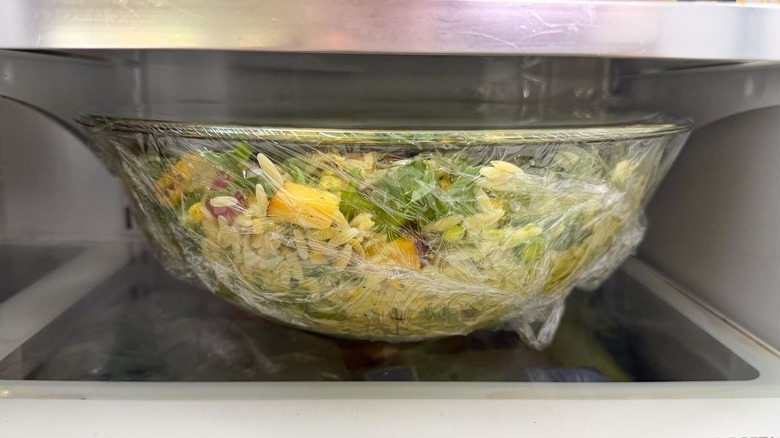 Summery grilled corn and orzo salad in plastic-covered glass bowl in refrigerator