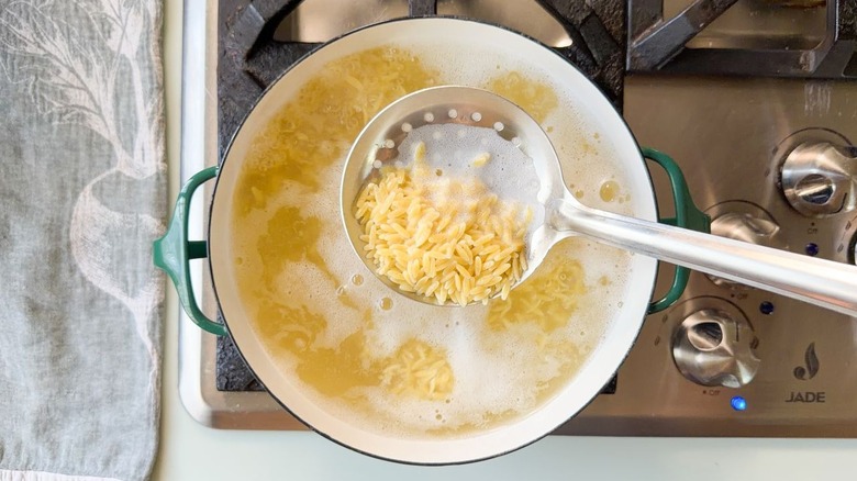 Orzo pasta cooking in pot on stovetop with slotted spoon