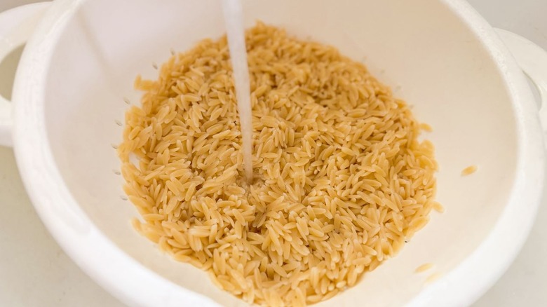 Rinsing cooked orzo with water in white colander in sink