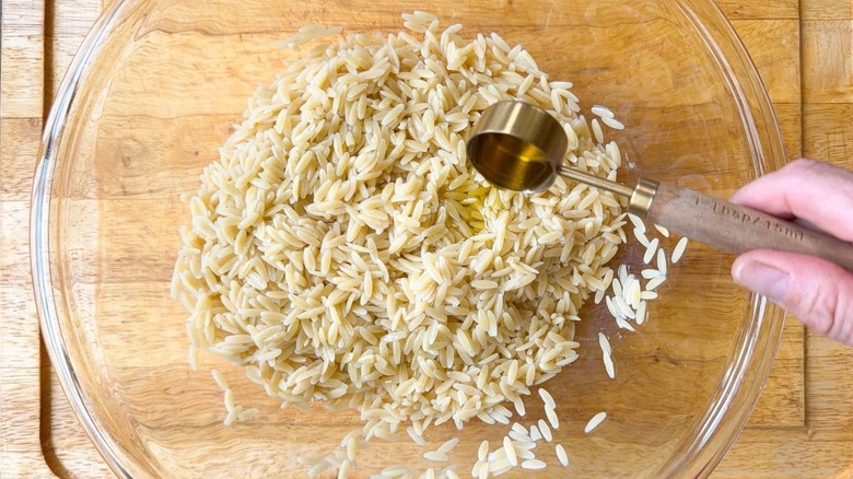 Adding olive oil to cooked orzo in large glass bowl