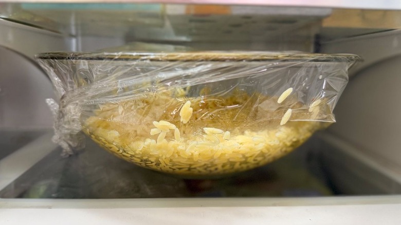 Cooked orzo in plastic-covered glass bowl in refrigerator