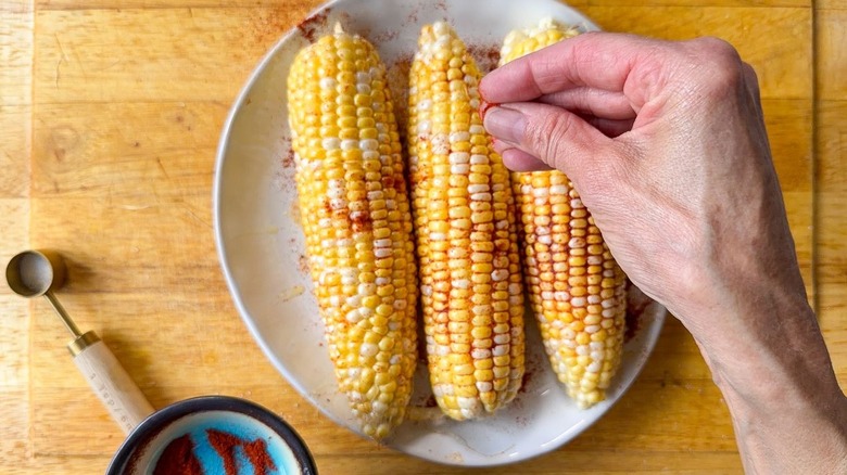 Sprinkling smoked paprika and salt on olive oil-coated corn on the cob