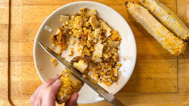 Cutting grilled corn kernels away from the cobs into a bowl
