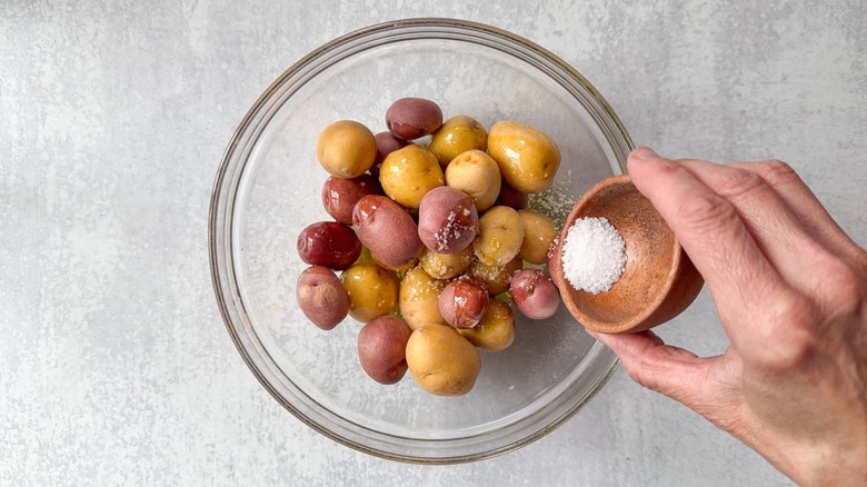 Mixing baby red and gold potatoes with olive oil and salt in glass bowl