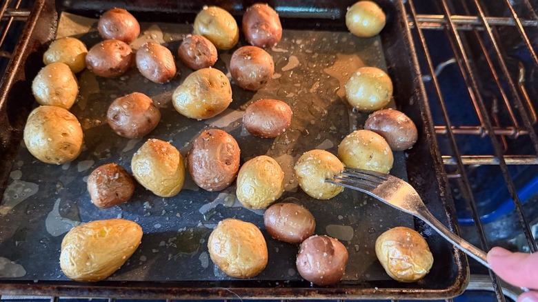 Baby red and gold potatoes on baking sheet in oven with fork test