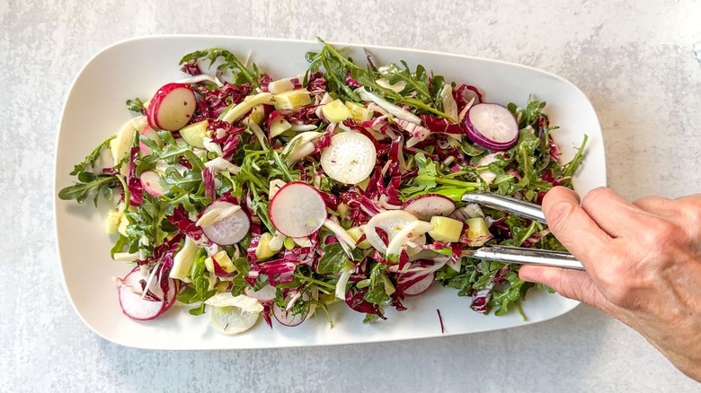 Salad greens and vegetables on white serving platter with tongs