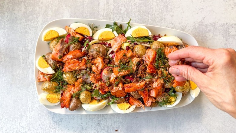 Adding capers and rye crumbs to summery hot-smoked salmon salad on serving platter