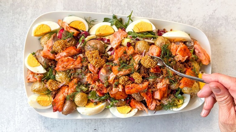 Adding pickled mustard seeds and red onions to summery hot-smoked salmon salad on serving platter