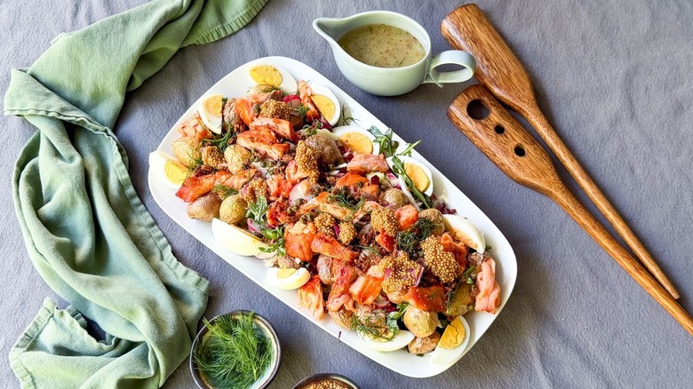 Summery hot-smoked salmon salad on table with dressing and serving spoons