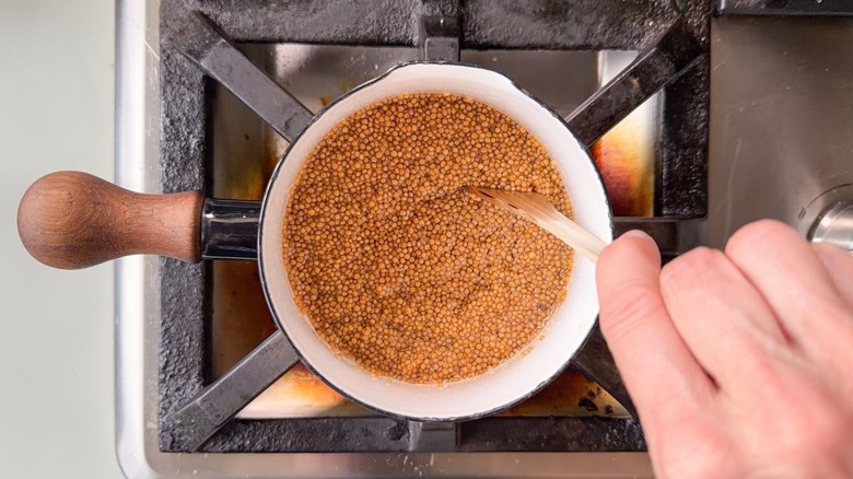 Stirring mustard seeds cooking in small saucepan with wooden spoon
