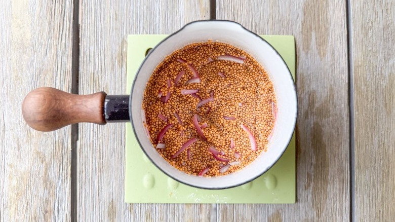Pickled mustard seeds and red onions cooling in small saucepan on trivet