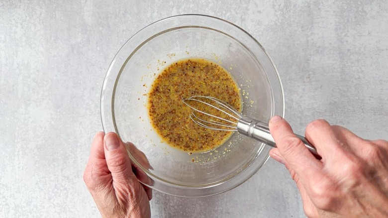 Whisking mustard, vinegar, sugar, and salt in glass bowl