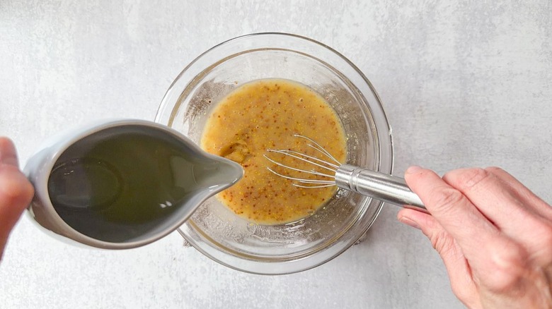 Drizzling and whisking oil into mustard dressing in glass bowl