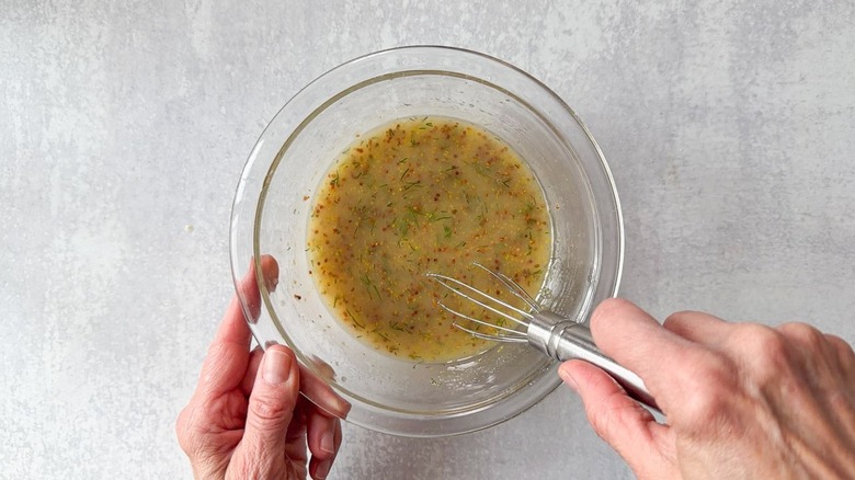 Whisking fresh chopped dill into mustard dressing in glass bowl