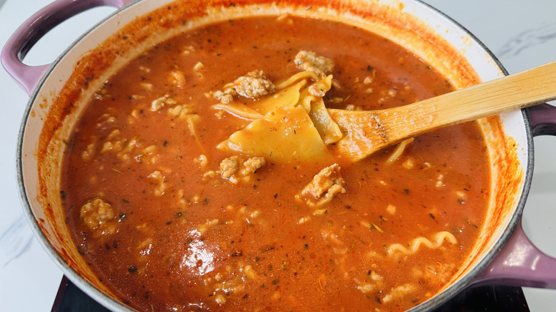 pot of tomato-noodle soup with a wooden spoon