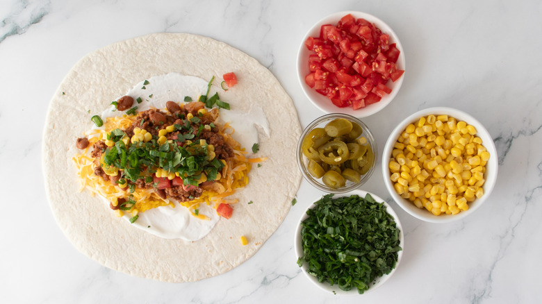 Large flour tortilla topped with corn, tomatoes, jalapeños, cilantro, and scallions