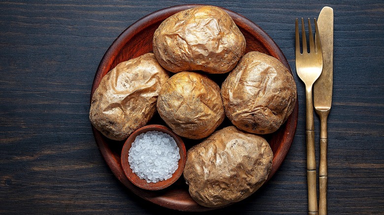 Whole baked potatoes and a small bowl of coarse salt in a shallow wooden bowl