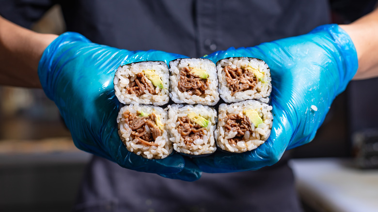 Six long sushi rolls held by hands in gloves
