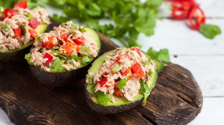 Tuna-stuffed avocados sit on a wooden board.
