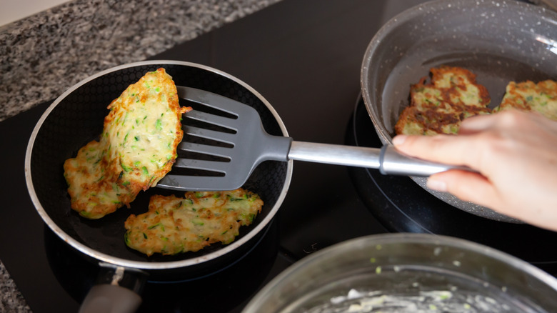 hand flipping a zucchini fritter in a non-stick pan