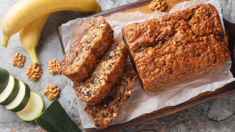 A loaf of banana bread with three slices arranged on a wooden board.