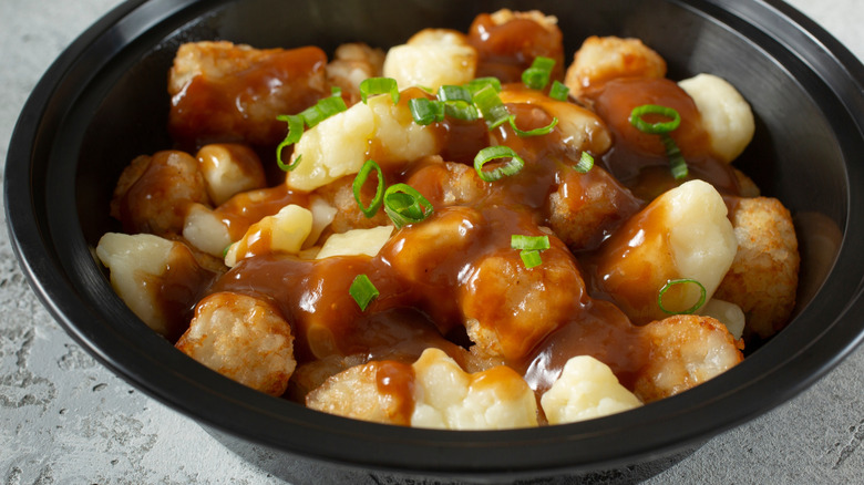 A closeup view of a bowl tater tots poutine in a takeaway container